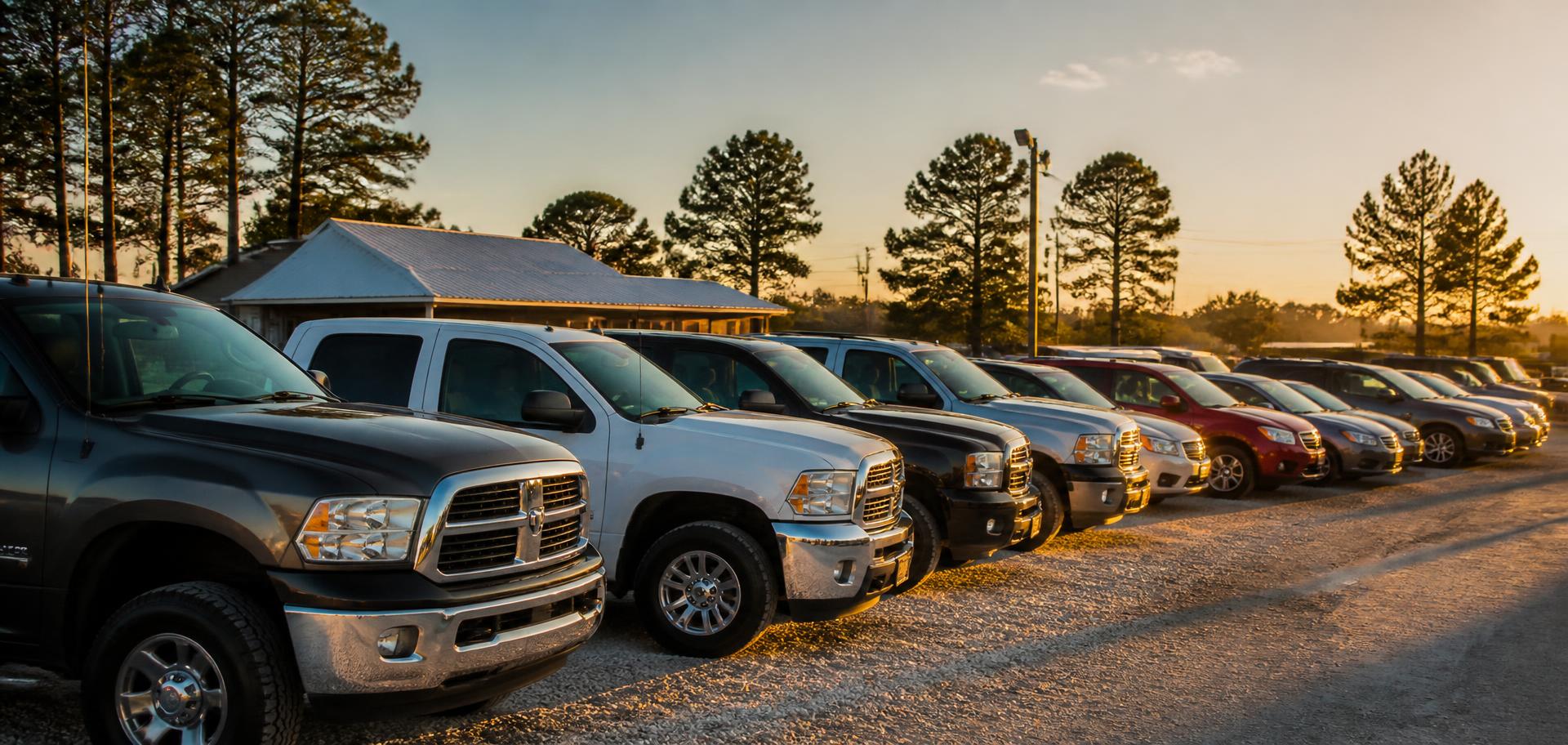 Row of pre-owned trucks, SUVs, and cars lined up on a Texas dealership lot at golden hour